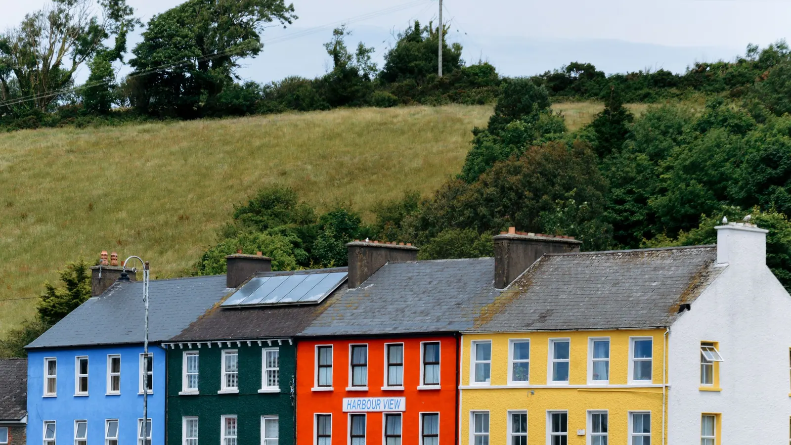 A row of blue, green, red and yellow terraced houses below a hillside in Bantry, County Cork